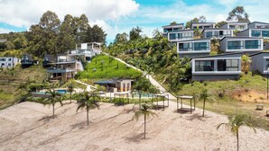 A hillside residential area with modern houses, a swimming pool, and a sandy beach. - Viajero Guatapé Hostel & Lake Club (El Peñol)