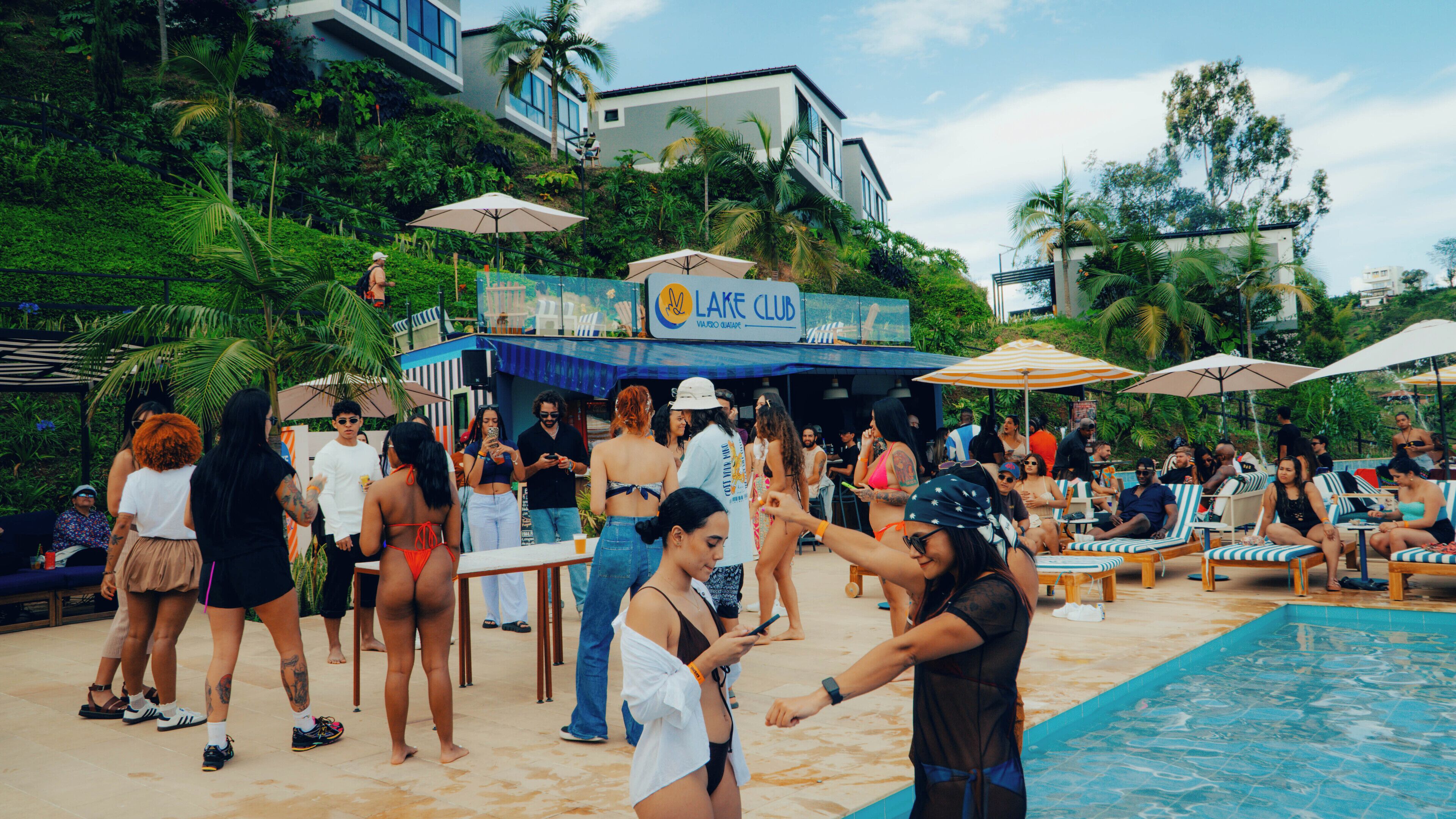 A poolside area with lounge chairs and umbrellas, a sign for 'Lake Club', and a crowd of people.