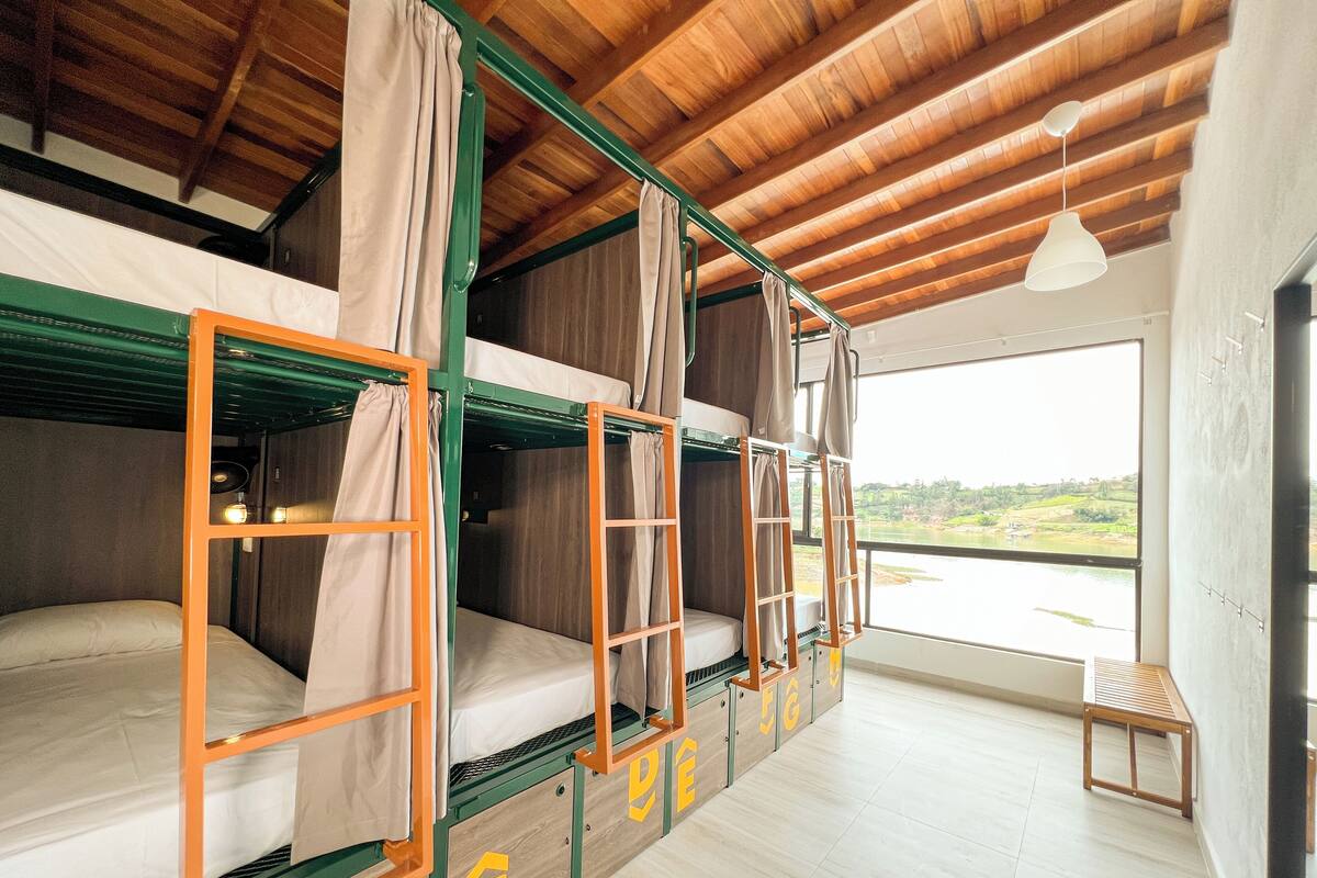 Une chambre de type dortoir, avec des lits superposés, un plafond en bois et une vue sur un paysage par la fenêtre.