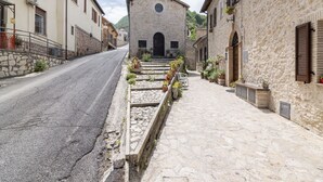 A narrow street with stone buildings, a church with a bell tower, and a row of potted plants along the sidewalk. - Belvilla by OYO Casa Angelica (Polino)