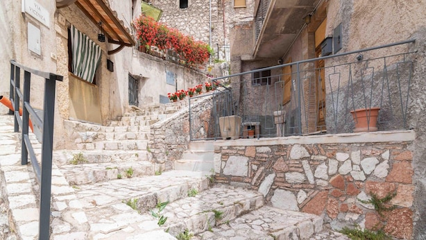 A stone staircase leading to a building with a balcony adorned with red flowers. - Belvilla by OYO Casa Angelica (Polino)