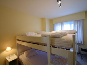 A bunk bed room with a nightstand, a lamp, and a window with curtains. - Apartment in De Haan Near the Beach (De Haan)