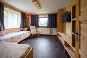 Ein Zimmer mit zwei Betten, einem Sessel, einem Fernseher und einem fenster mit Vorhängen.