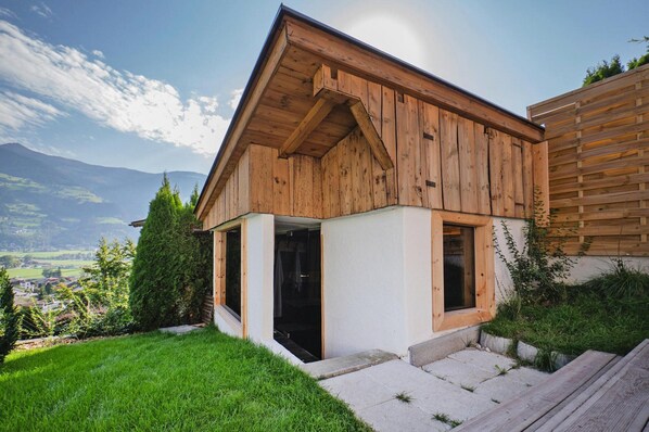 A wooden house with a sloped roof, large windows, and a view of a valley.