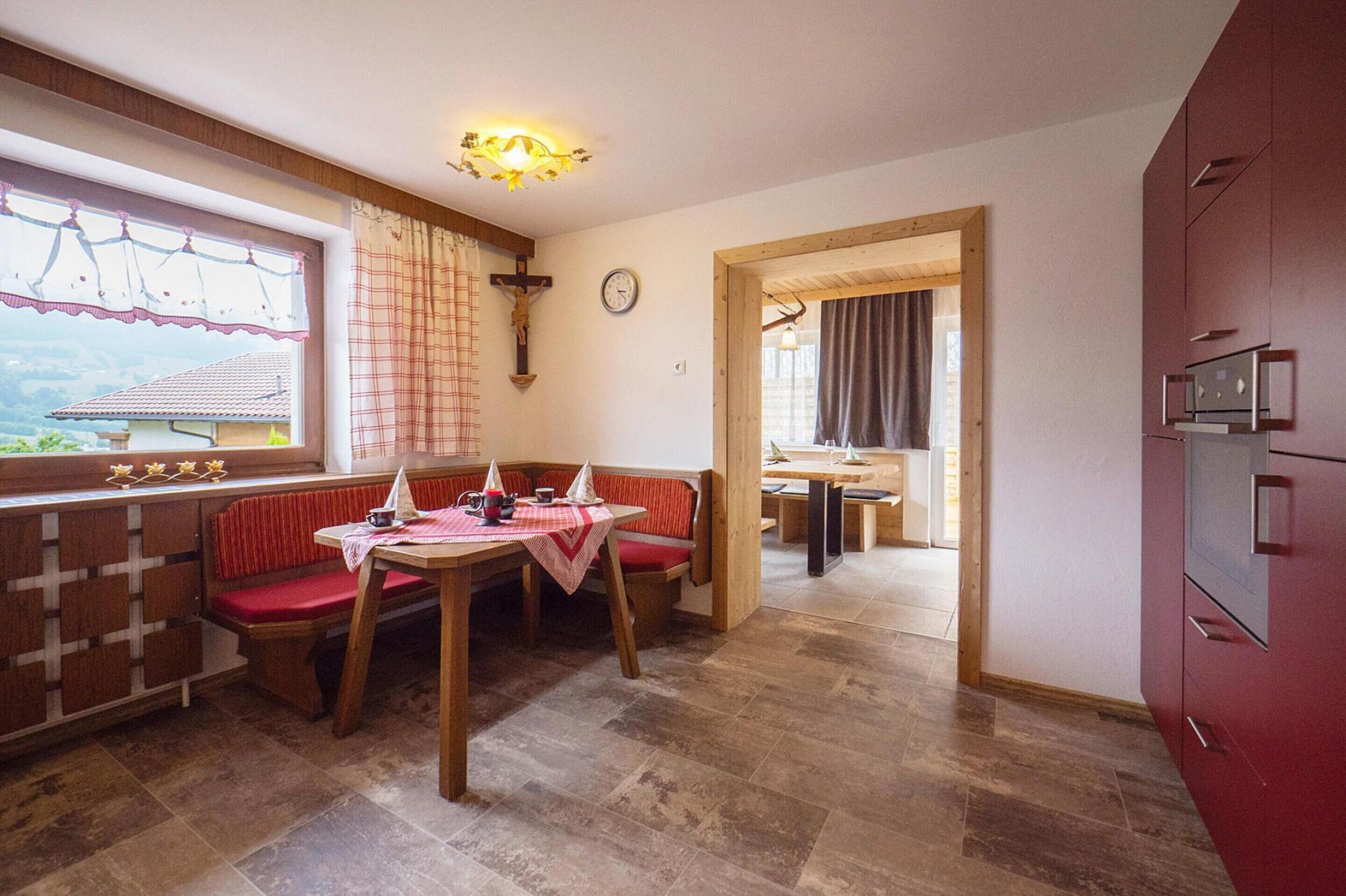 Un comedor con una mesa y banco de madera, una ventana con vistas, un reloj y un armario rojo.