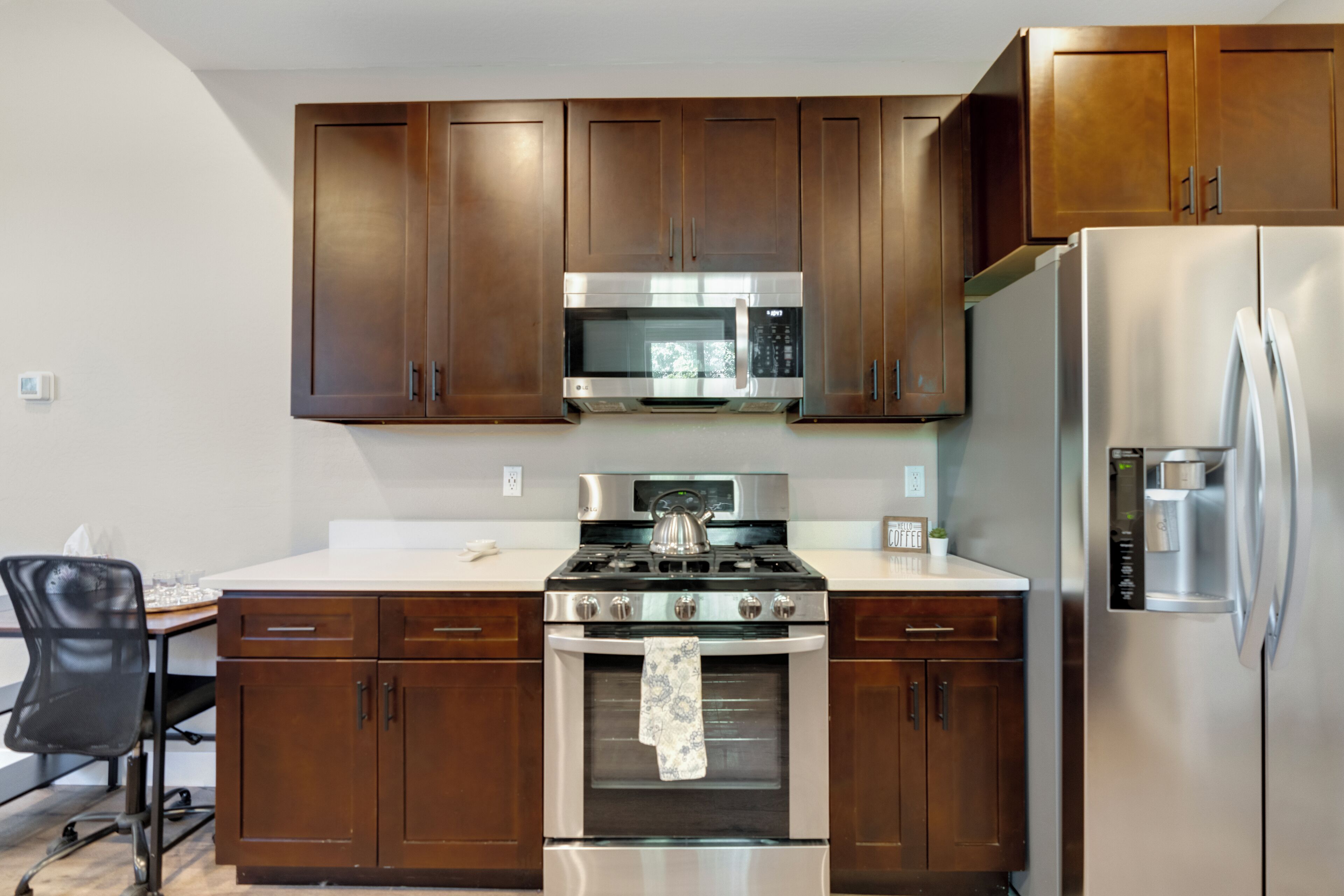 A modern kitchen with wooden cabinets, stainless steel appliances, and a black office chair.