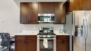 A modern kitchen with wooden cabinets, stainless steel appliances, and a black office chair.