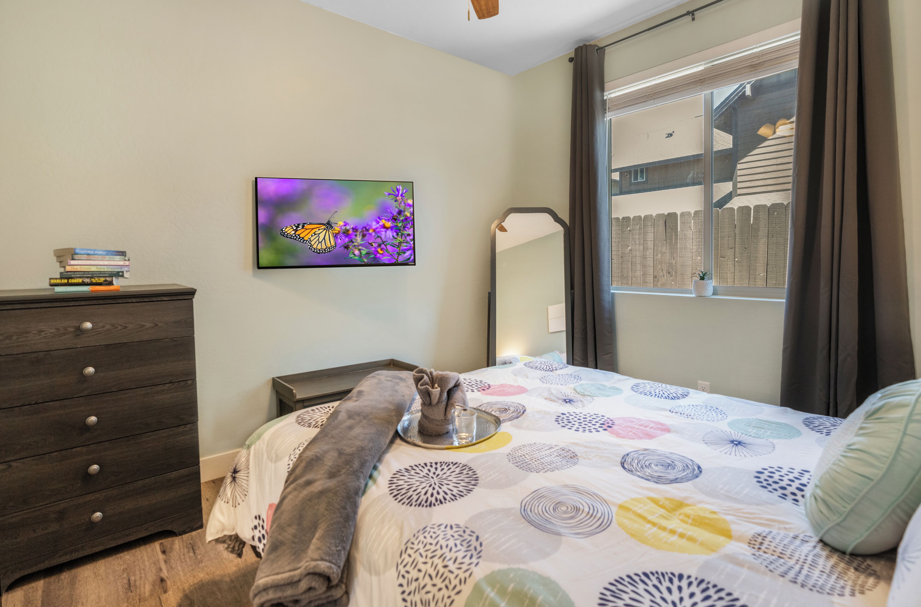 A bedroom with a bed, a dresser, a painting, and a window with a view of a fence.