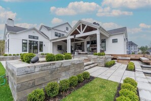 Une grande maison de plain-pied dotée d’un patio couvert, d’une cheminée en pierre et d’une pelouse bien entretenue.