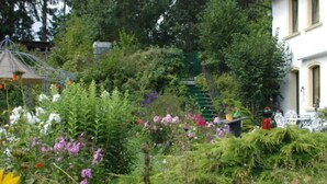 A garden with a variety of plants and flowers, a gazebo, and a building with a staircase. - Holiday Apartment Alpakahof Blomberg (Meinerzhagen)