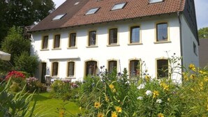 A two-story house with a tiled roof, multiple windows, and a well-maintained garden with various flowers. - Holiday Apartment Alpakahof Blomberg (Meinerzhagen)