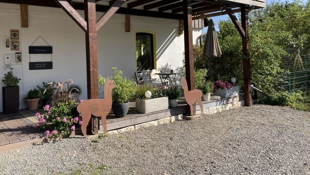 A covered outdoor area with wooden beams, potted plants, and a gravel path. - Holiday Apartment Alpakahof Blomberg (Meinerzhagen)