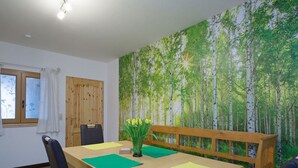 A dining area with a wooden table, chairs, and a bench. A forest mural decorates the wall behind the table. - Holiday Apartment Alpakahof Blomberg (Meinerzhagen)