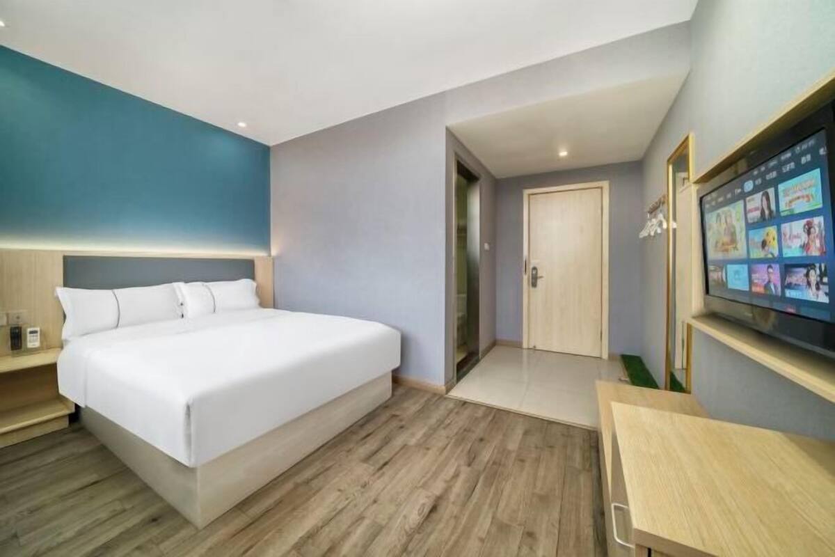 A modern hotel room with a large bed, a desk, a TV, and a door leading to another room.