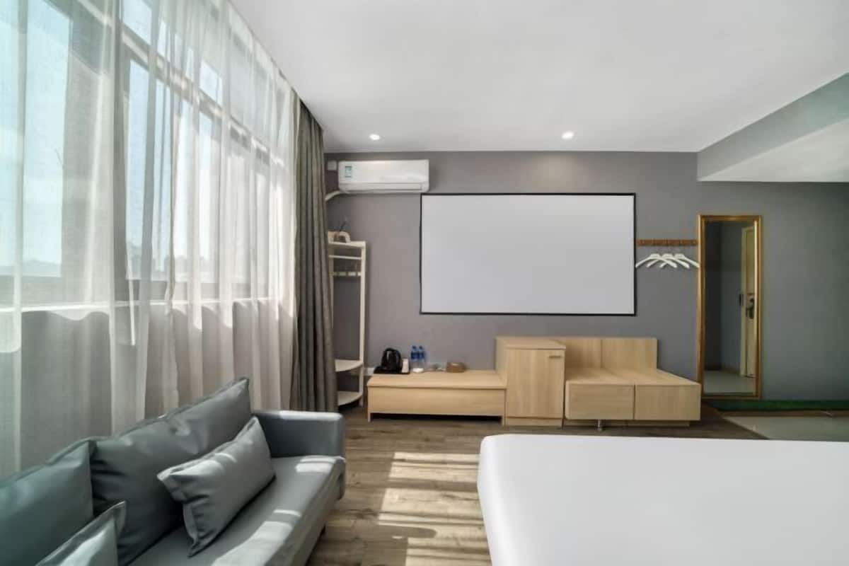 A modern hotel room with a large bed, a sofa, a desk, and a large window with curtains.