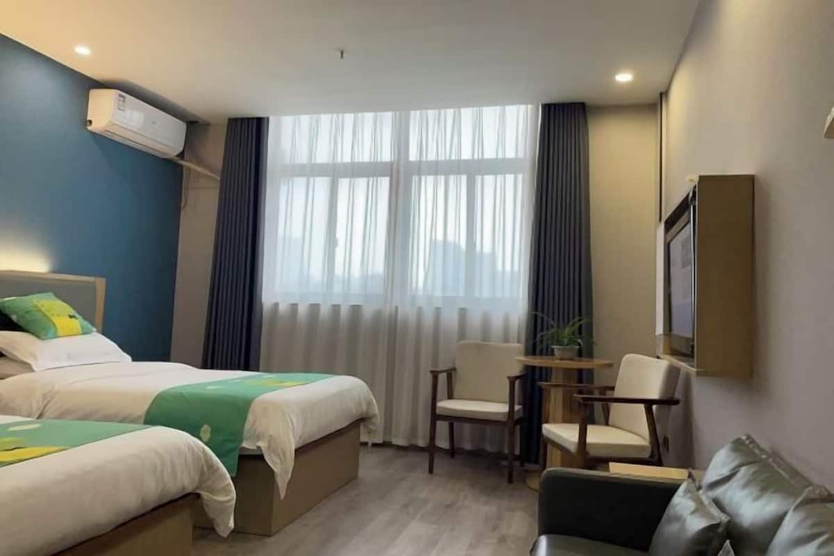 A hotel room with two beds, a desk, a chair, a sofa, and a large window with curtains.
