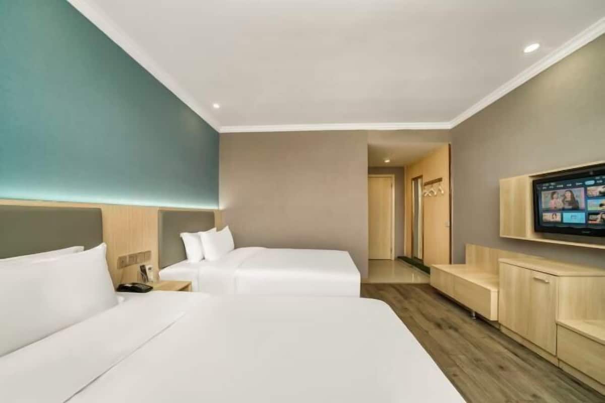 A hotel room with two beds, a TV, and a wooden bench.