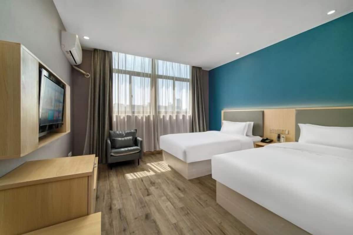 A hotel room with two beds, a TV, a chair, and a wooden floor.