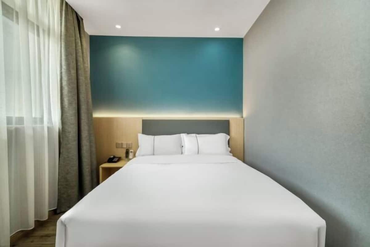 A hotel room with a large bed, a nightstand, and a wall-mounted lamp.