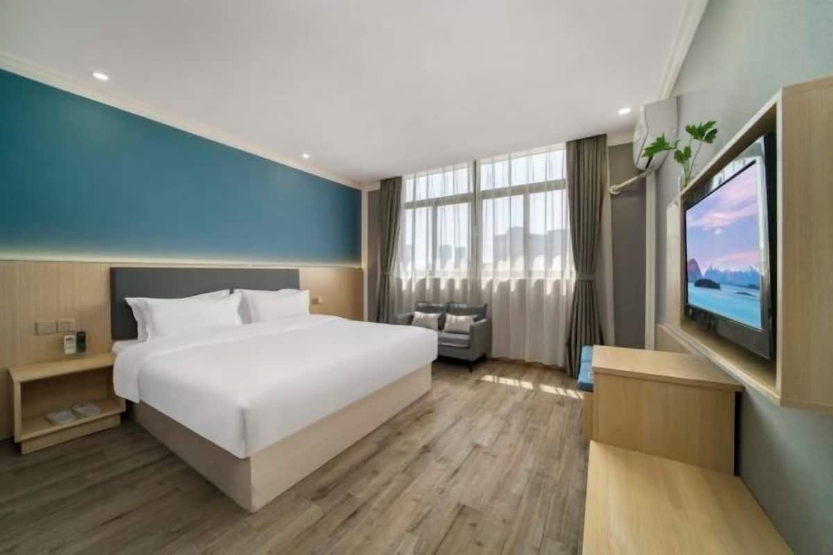 A hotel room with a large bed, a TV, a desk, and a window with curtains.
