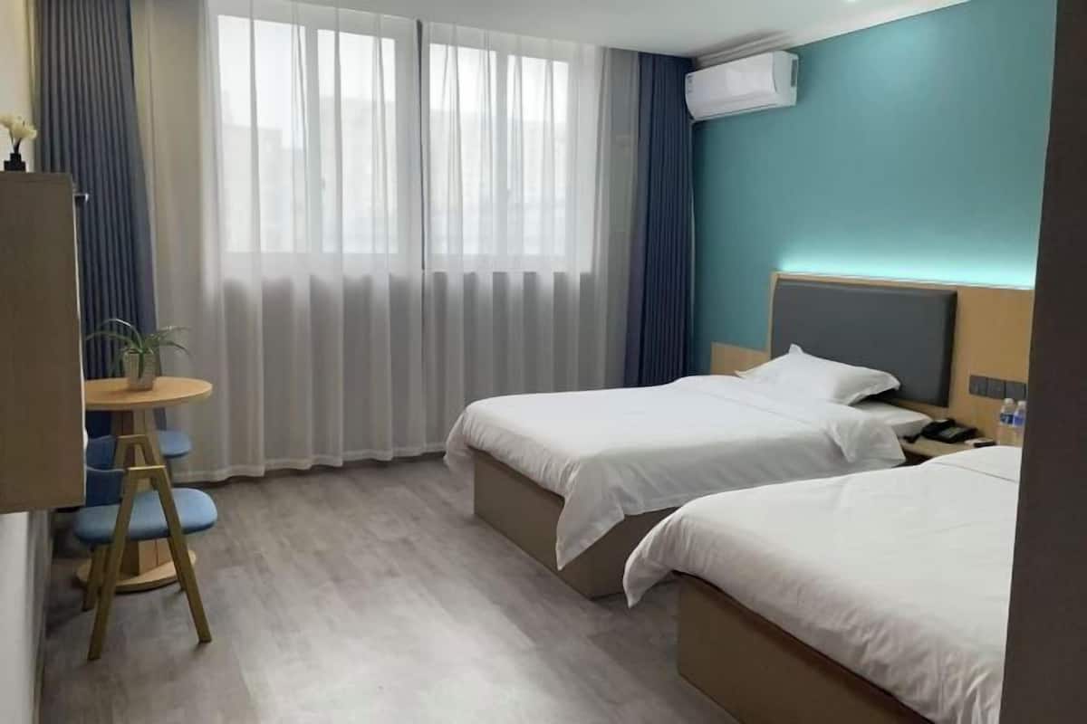 A hotel room with two beds, a desk, a chair, and a window with curtains.