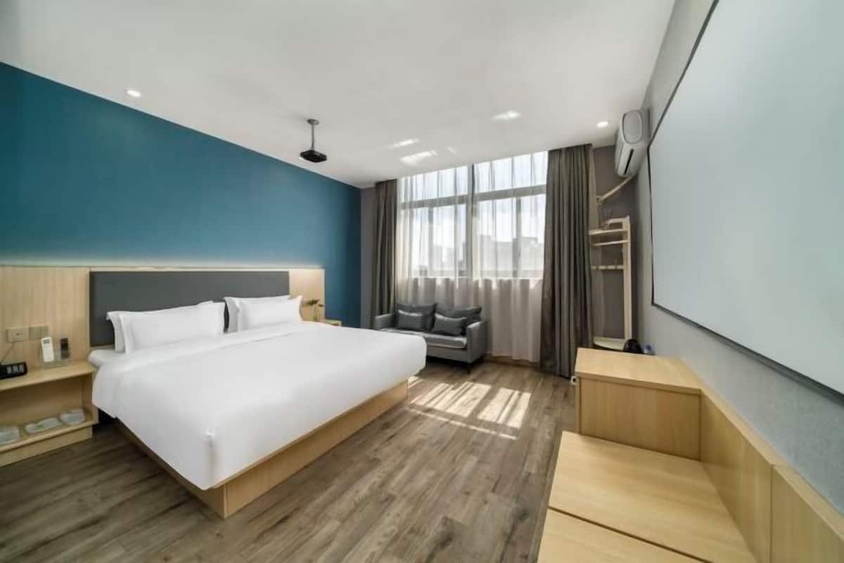 A modern hotel room with a large bed, a seating area, a wardrobe, and a large window.