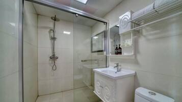 A modern bathroom with a glass-enclosed shower, a white sink, and a toilet.