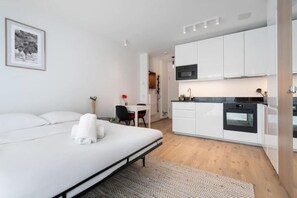 Een moderne hotelkamer met een bed, een klein bureau, een kitchenette en een eethoek.