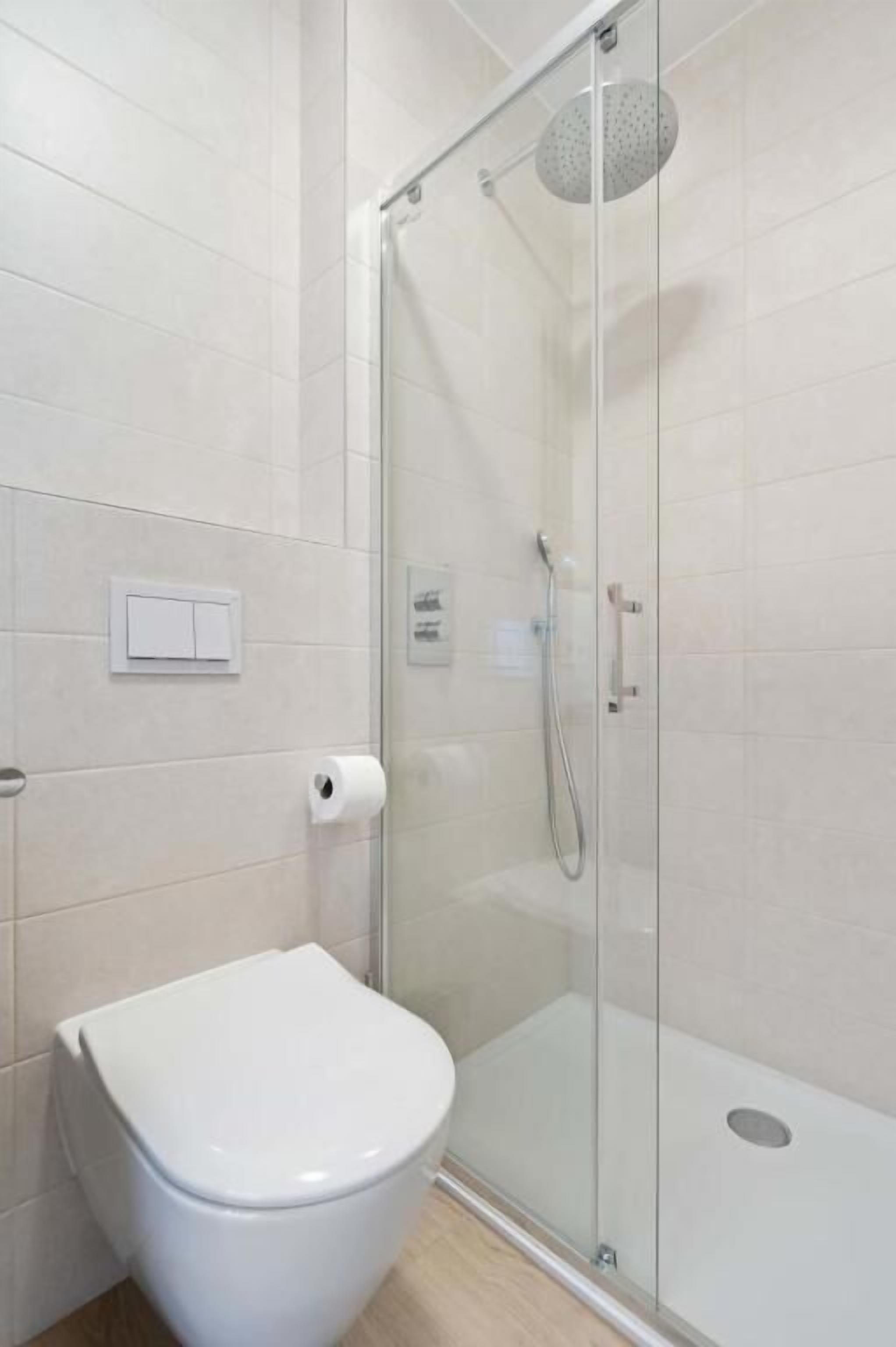 Un baño moderno con ducha de vidrio, inodoro blanco y un sistema de descarga en la pared.