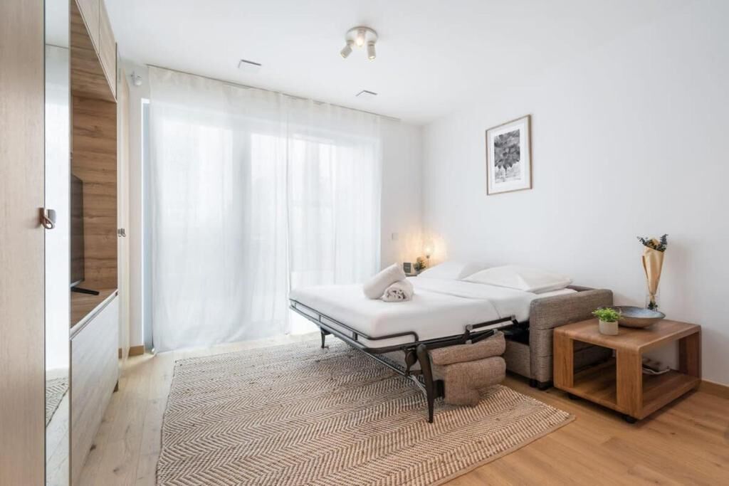 Un dormitorio moderno con cama, mesita de noche y vistas a un paisaje urbano a través de amplias ventanas.