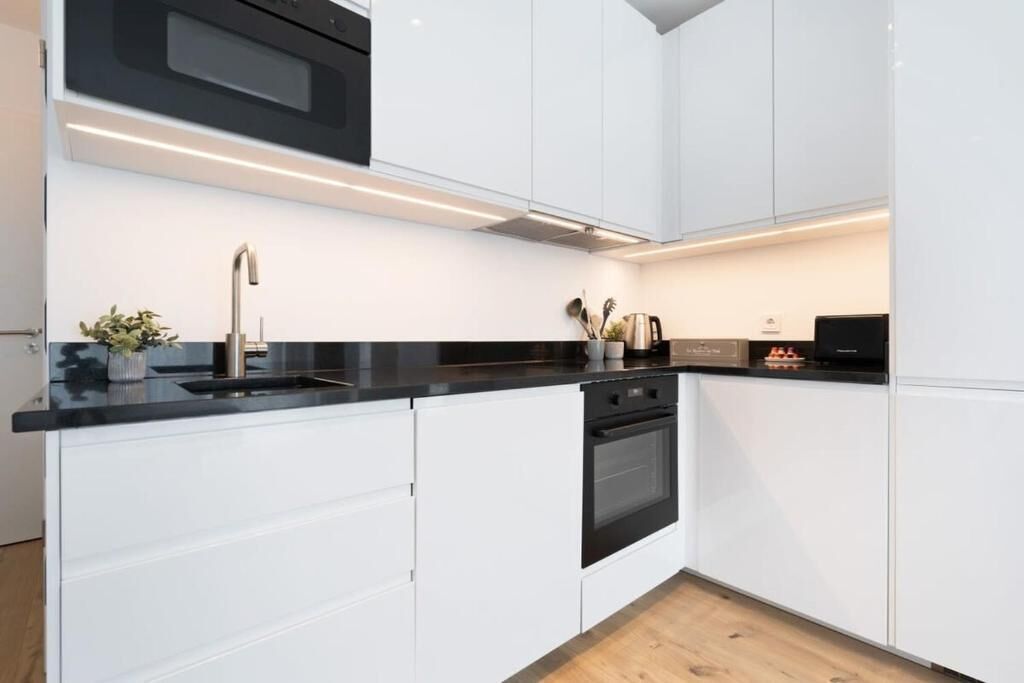 A modern kitchen with white cabinetry, a black countertop, and stainless steel appliances.