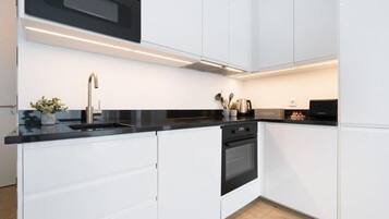 A modern kitchen with white cabinetry, a black countertop, and stainless steel appliances.