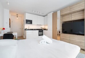 Een moderne hotelkamer met een groot bed, een flatscreen televisie aan de muur, een kitchenette en een bureau met een stoel.