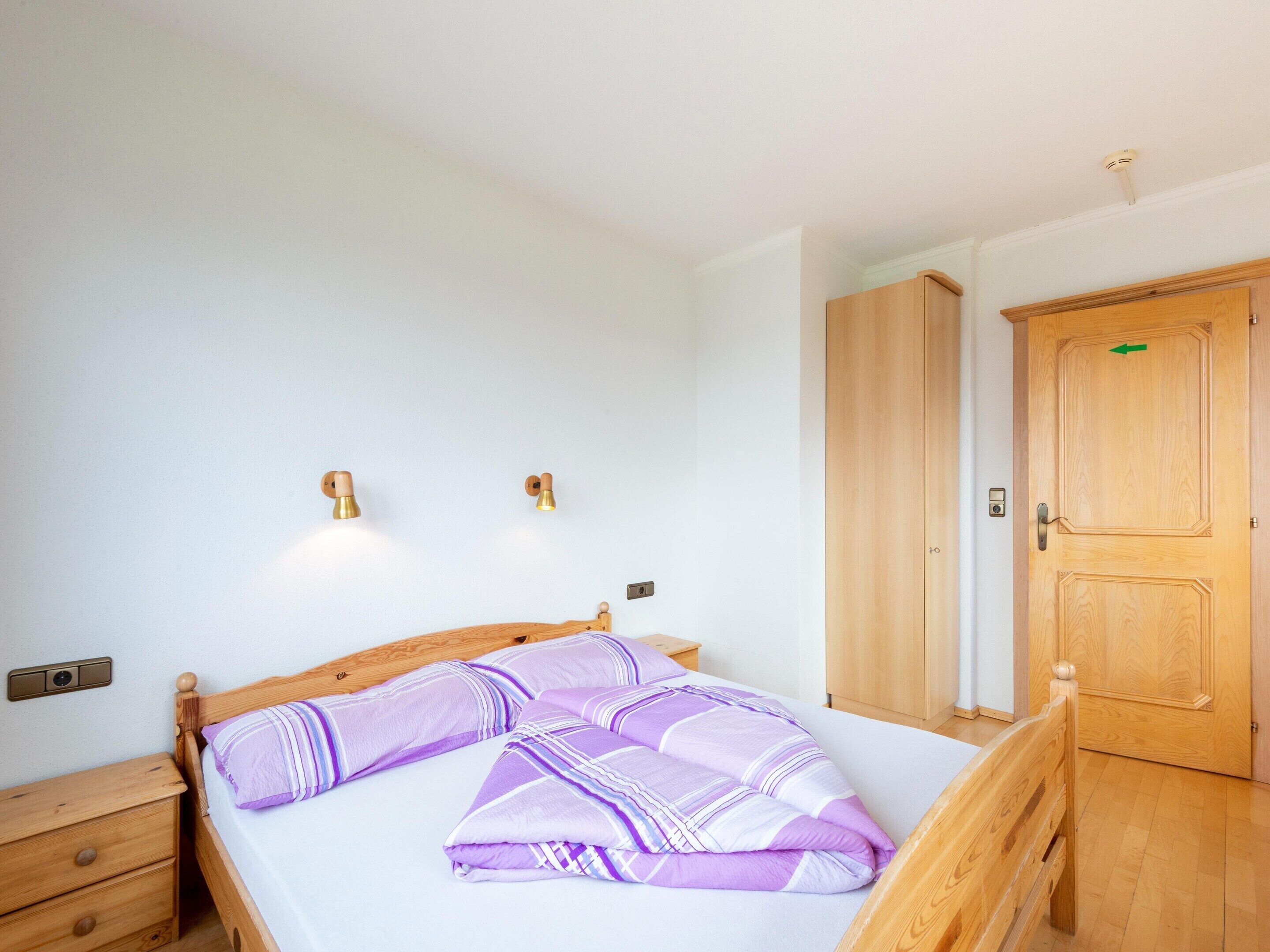 A bedroom with a wooden bed, a nightstand, a wardrobe, and two wall-mounted lights.