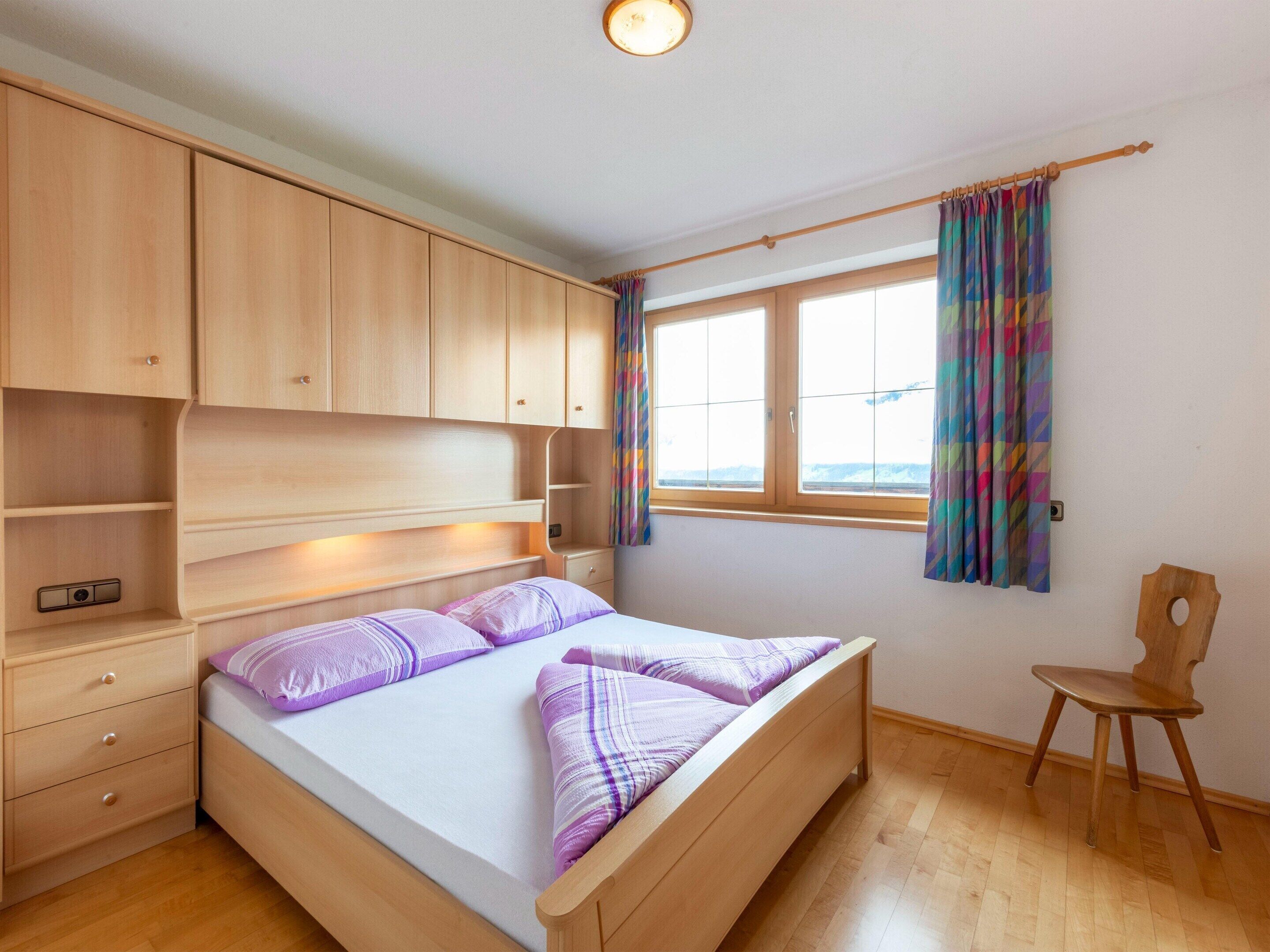 A bedroom with a bed, wooden wardrobe, bedside table, and a window with curtains.