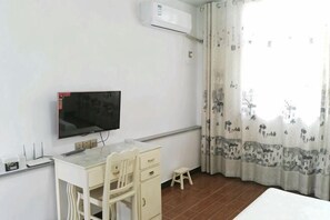 A room with a TV mounted on the wall, a desk with a chair, a small stool, and a bed. - Xiuning Yuanyuan Hotel (Xiuning)