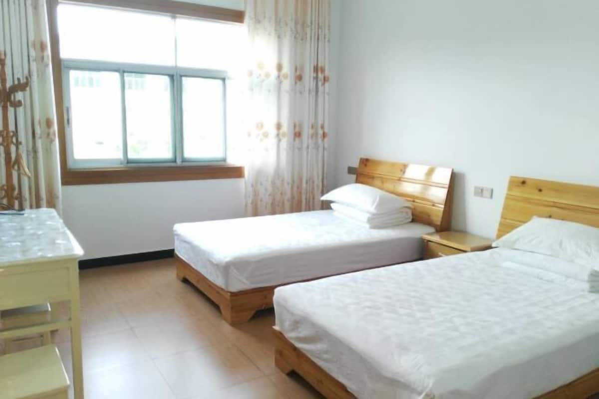 A bedroom with two single beds, a wooden headboard, a bedside table, and a window with curtains.