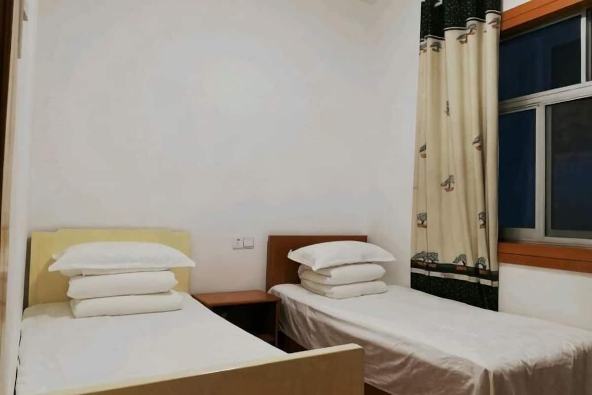 A small, clean room with two single beds, a window with curtains, and a wooden headboard.
