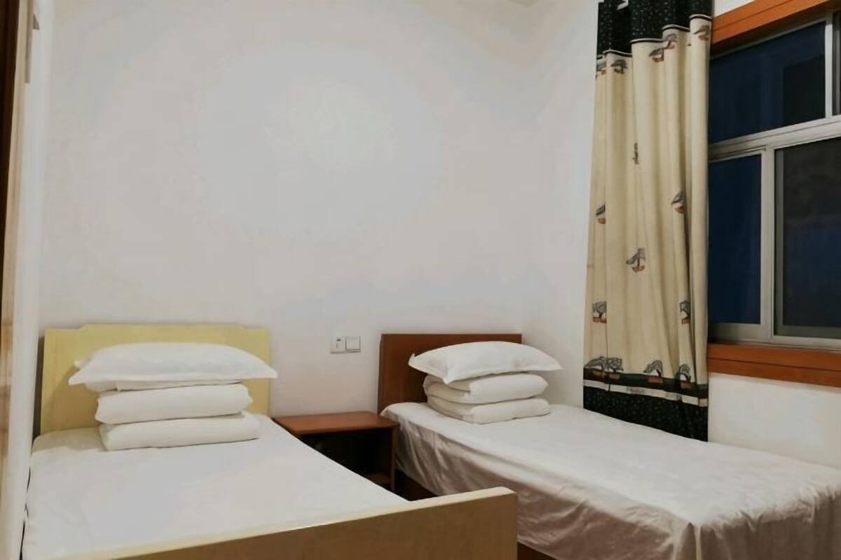 A small, clean room with two single beds, a window with curtains, and a wooden headboard.