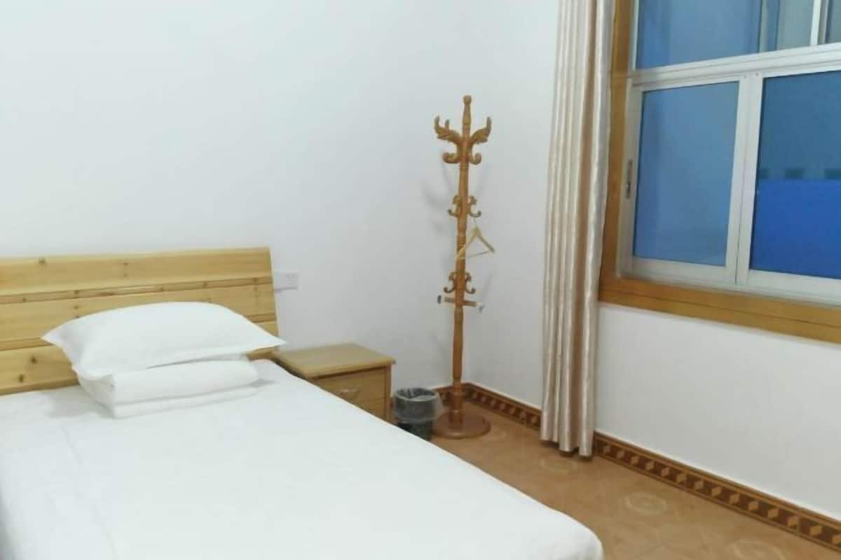 A bedroom with a wooden headboard, a bed with white bedding, a small bedside table, a waste bin, and a coat stand.