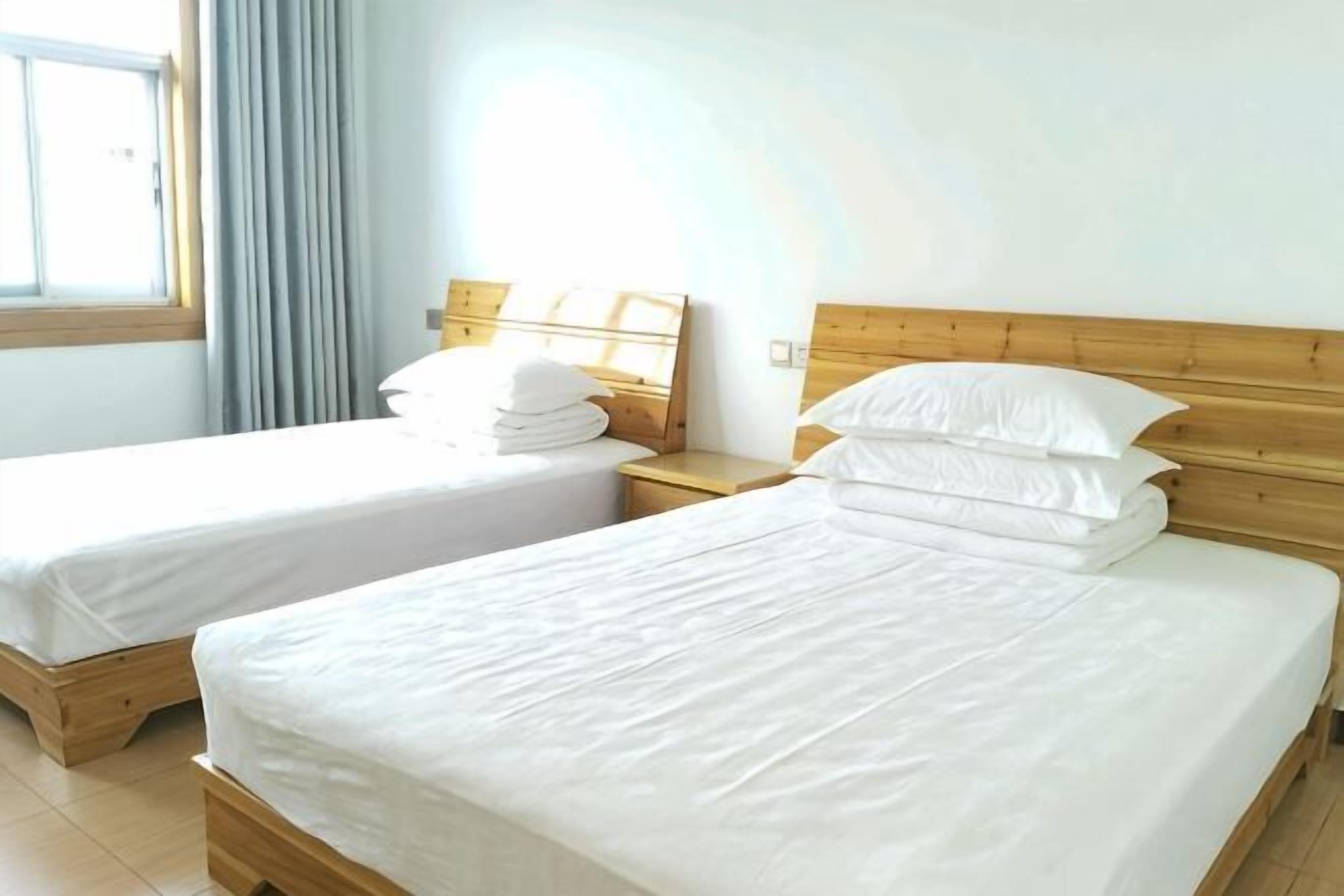 Two single beds with wooden headboards, white bedding, and a window with curtains.