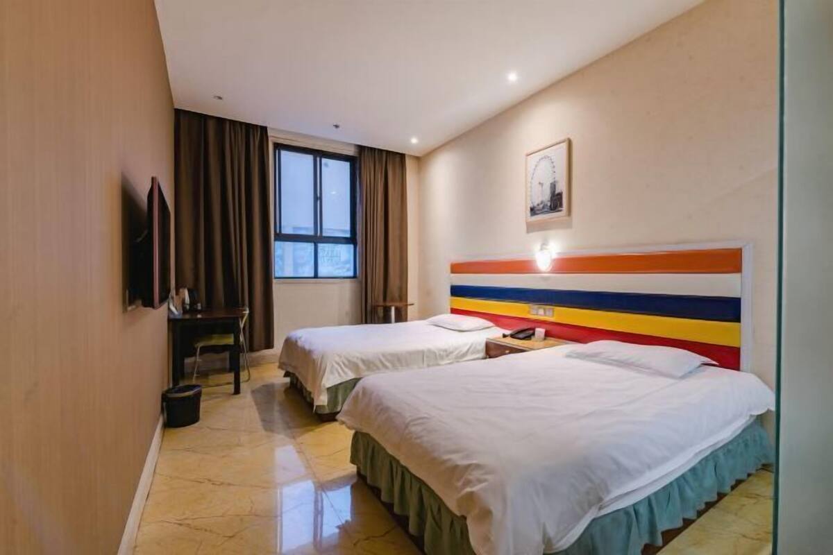 A hotel room with two beds, a desk, a chair, a TV, and a window with curtains.