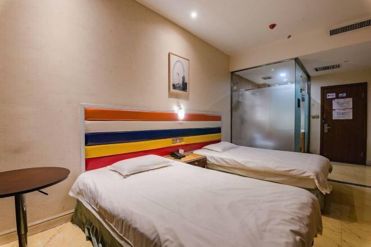 A hotel room with two beds, a small table, a mirror, and a door with a sign.