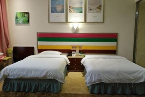 Hotellihuone, jossa on kaksi sänkyä, kirjoituspöytä lampun kanssa ja seinällä on kehystettyjä kuvia.