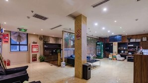 Eine Hotelhalle mit einer Rezeption, einer Sitzecke und einem großen Bildschirm.