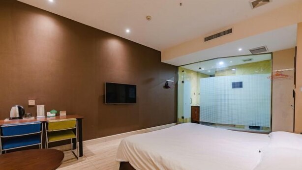 Ein Hotelzimmer mit Bett, Schreibtisch mit Stühlen, Fernseher und einem durch eine Glastür einsehbaren Badezimmer.