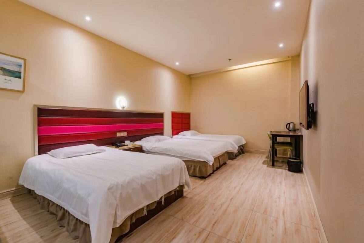 A hotel room with two beds, a wooden headboard, a small table with a kettle, and a TV mounted on the wall.