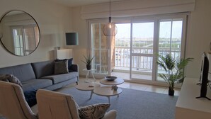 Un salon moderne avec un canapé gris, deux fauteuils, une table basse et un balcon offrant une vue sur la ville.