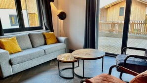 Een moderne woonkamer met een grijze bank, twee ronde houten tafels en een fauteuil.