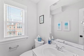 A modern bathroom with a large window, a white sink, and two framed pictures on the wall. - Aviation Themed Townhome w/ Waterpark & Game Room - Pet Friendly (Kill Devil Hills)
